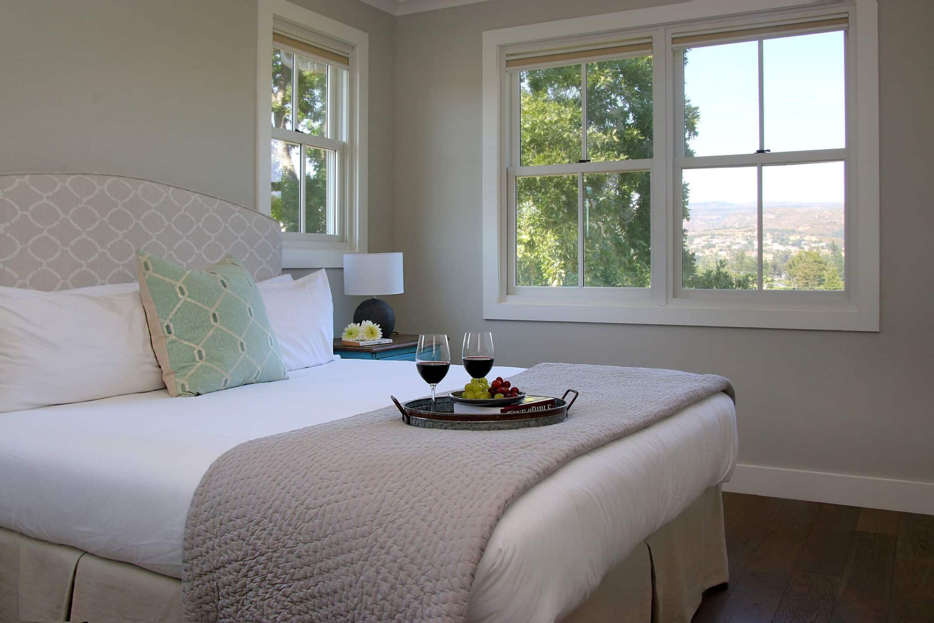 A bed with a tray of food and wine on it