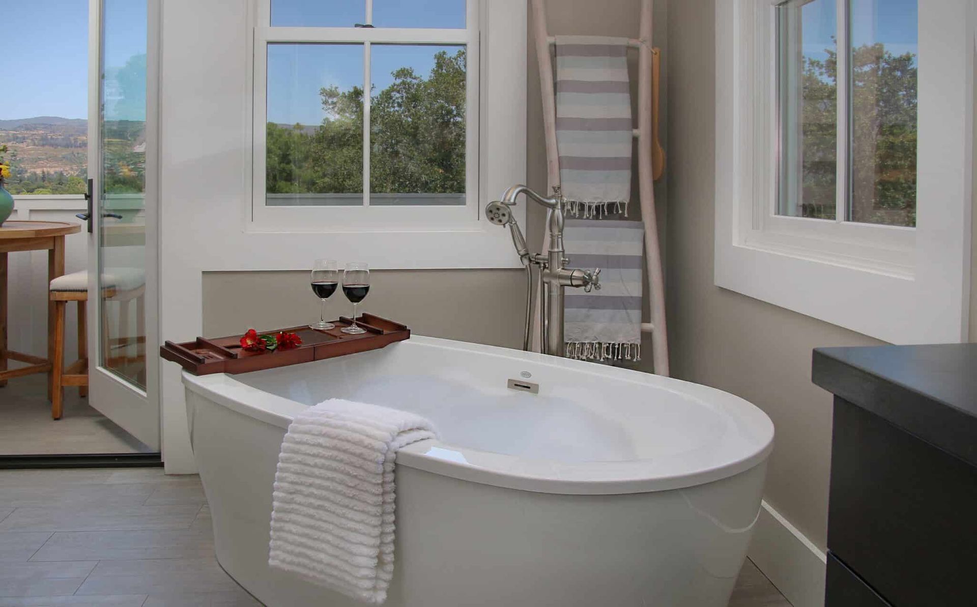 A bathroom with a bathtub and two glasses of wine on a tray.