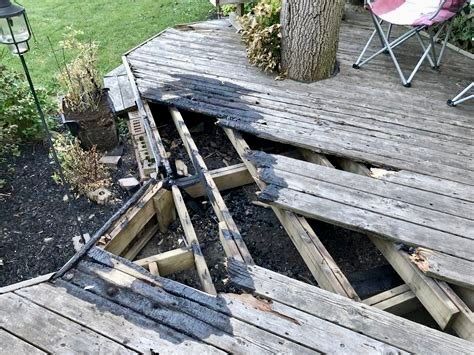 Broken wooden deck sagging around a tree trunk, with exposed supports and missing boards in a yard.