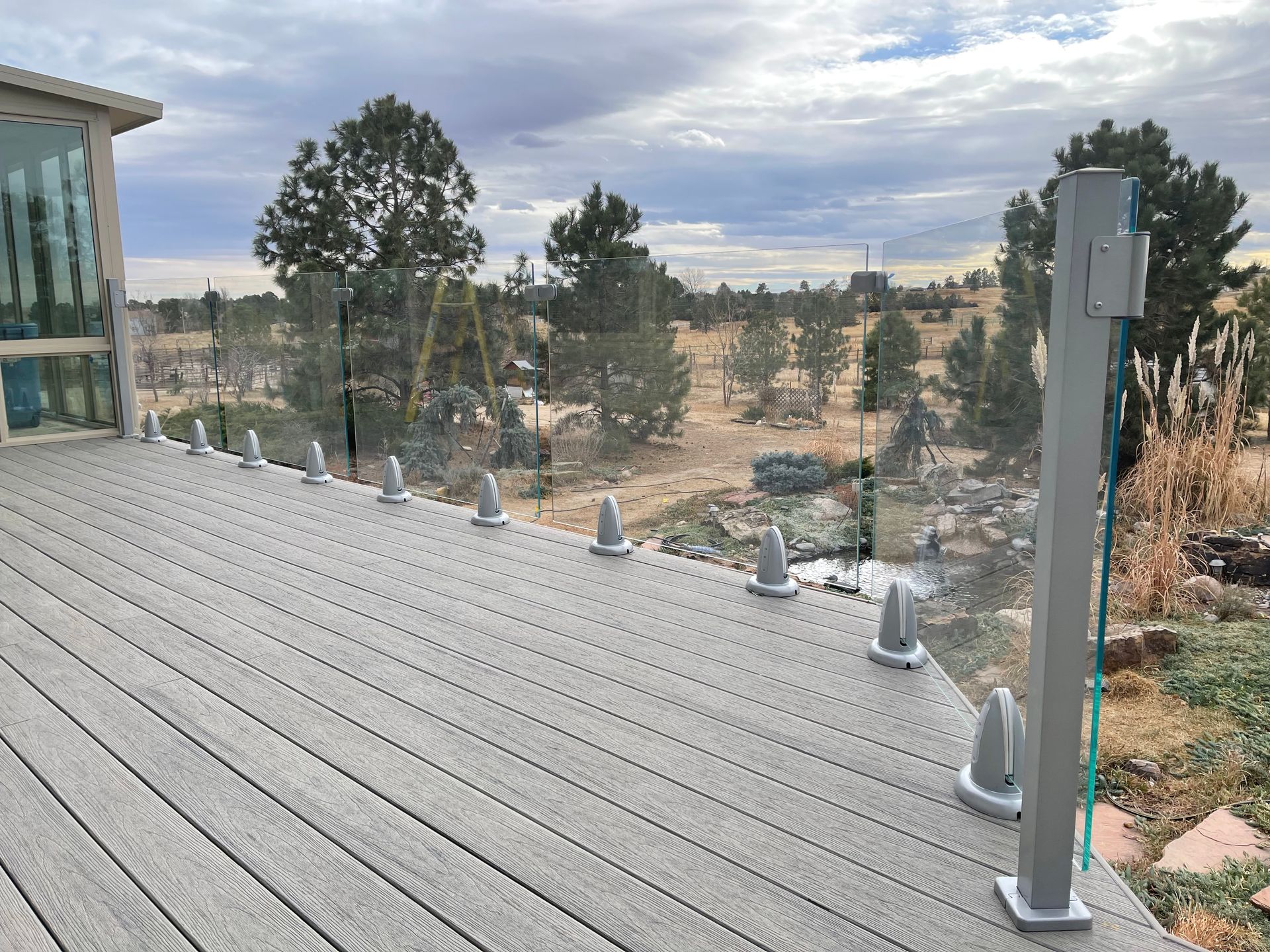 A wooden deck with a glass railing and trees in the background.