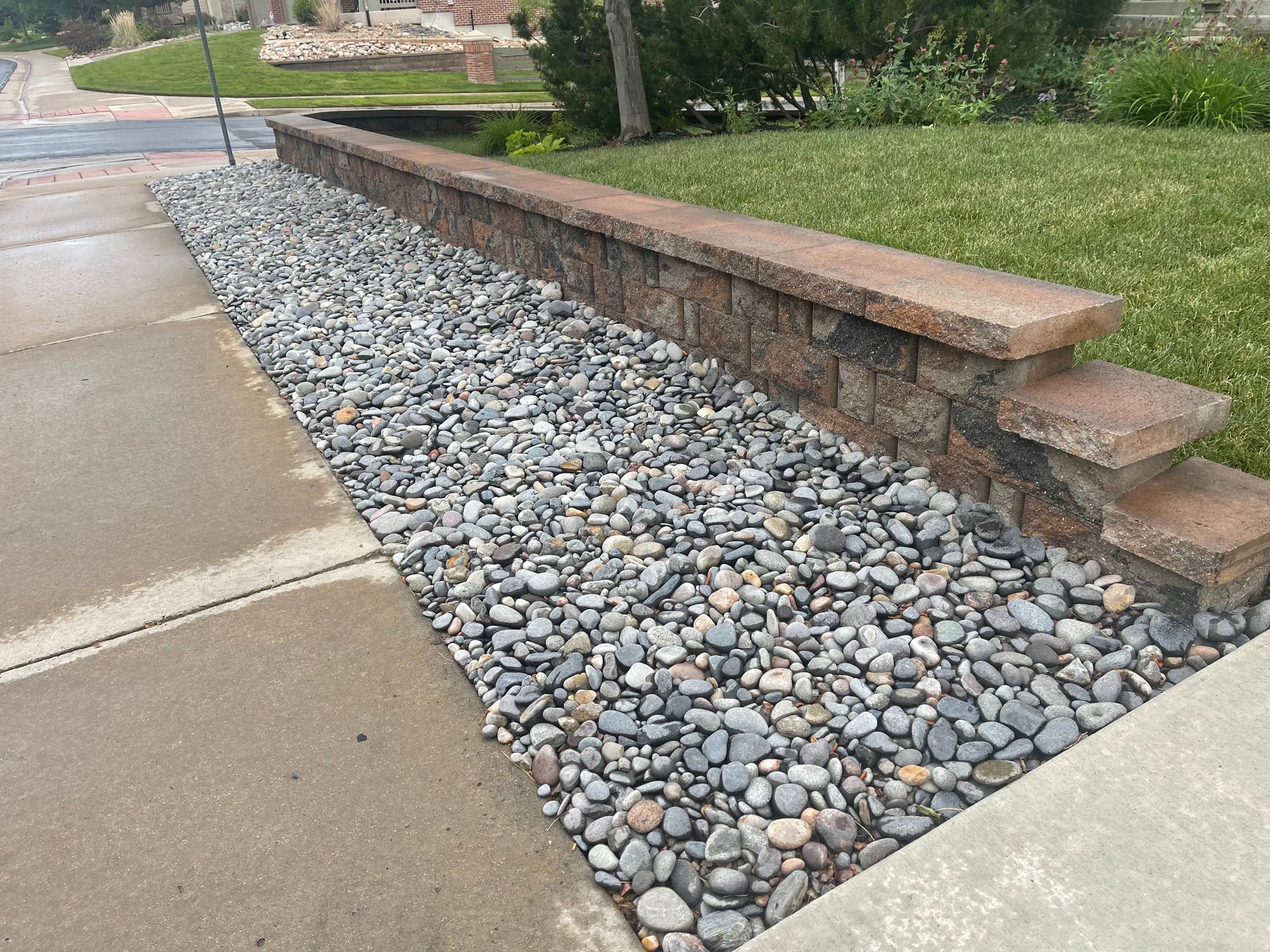A stone wall surrounded by gravel next to a sidewalk.
