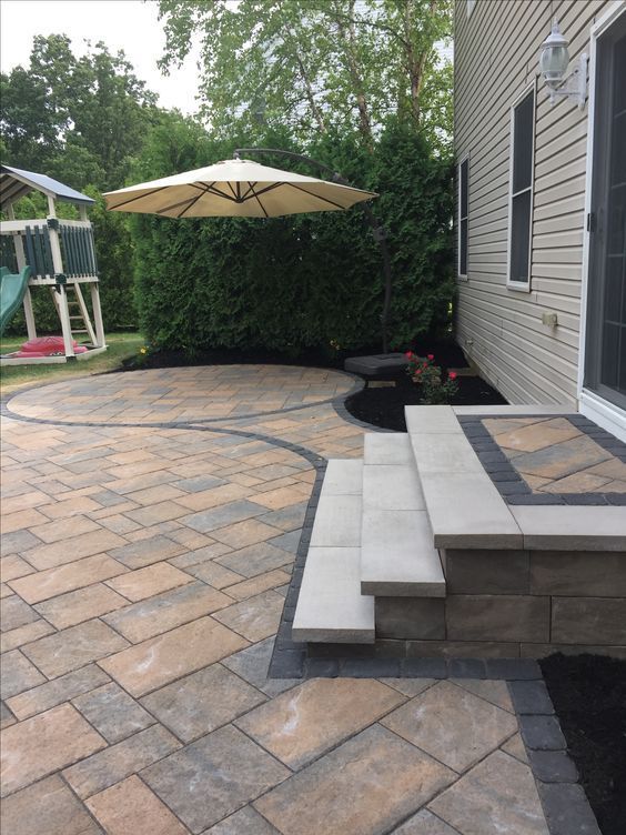 A patio with a umbrella and steps in front of a house.