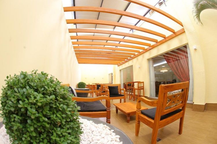 Pátio coberto com móveis de madeira, pérgola arqueada e plantas em vasos, em uma área de estar externa bem iluminada.