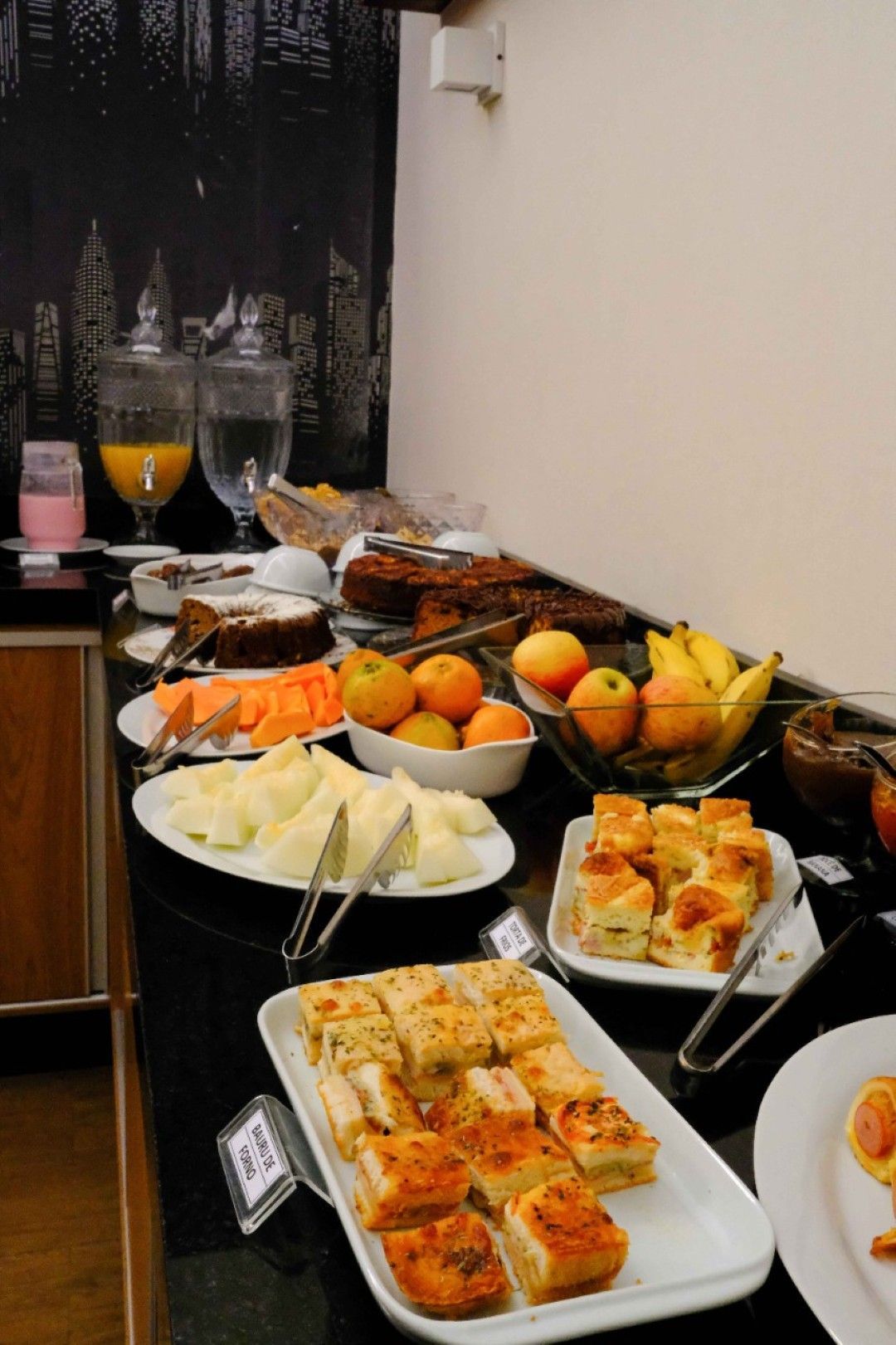 Mesa de buffet com doces, frutas e bebidas em uma sala de jantar.