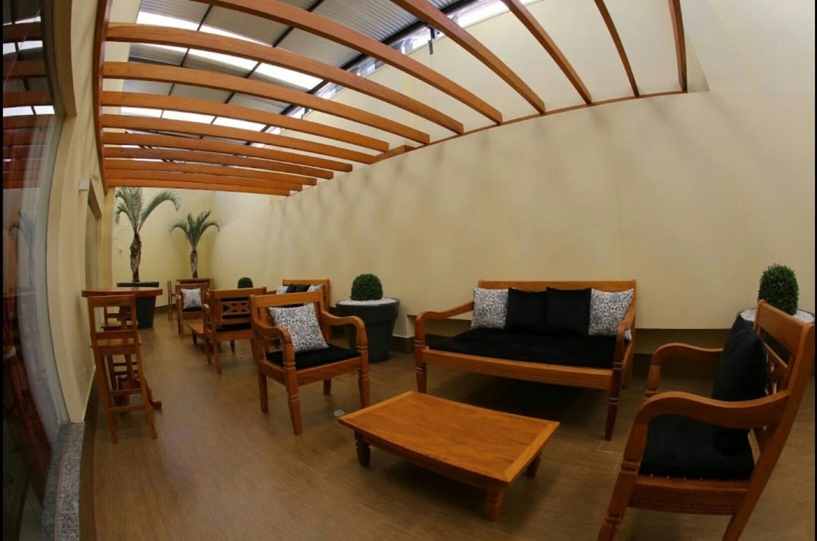 Sala de estar moderna com móveis de madeira, teto arqueado, plantas em vasos e iluminação aconchegante.