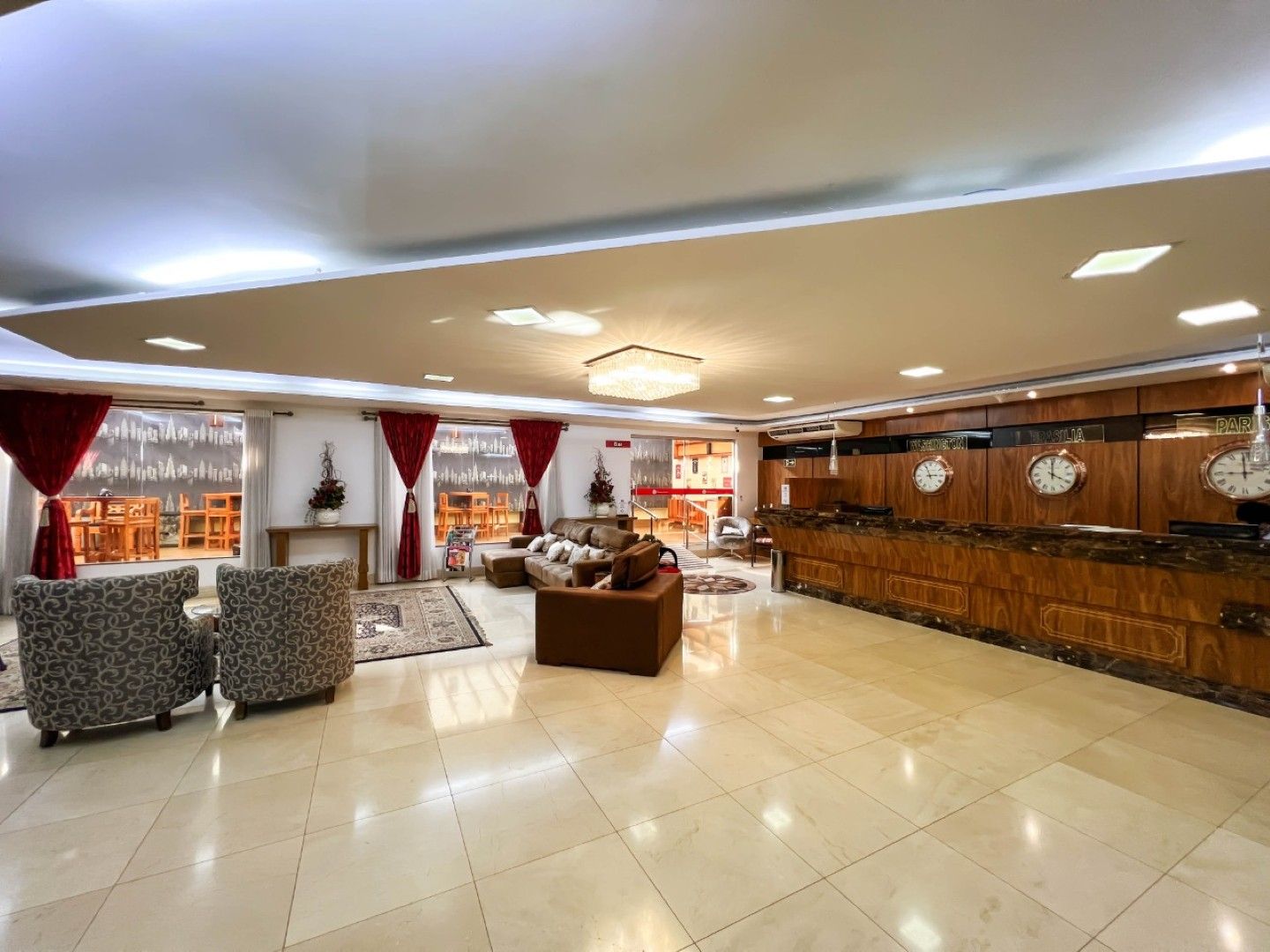 Hall de entrada elegante do hotel com piso de azulejos, cadeiras estampadas, balcão de recepção e bar com painéis de madeira.