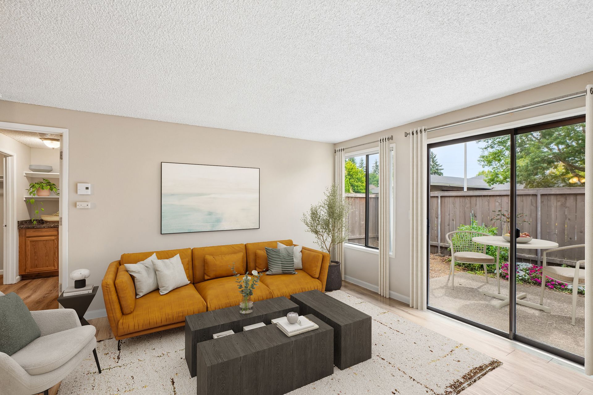 Bright living room with mustard sofa, dark ottomans, wall art, and sliding glass doors to a patio.