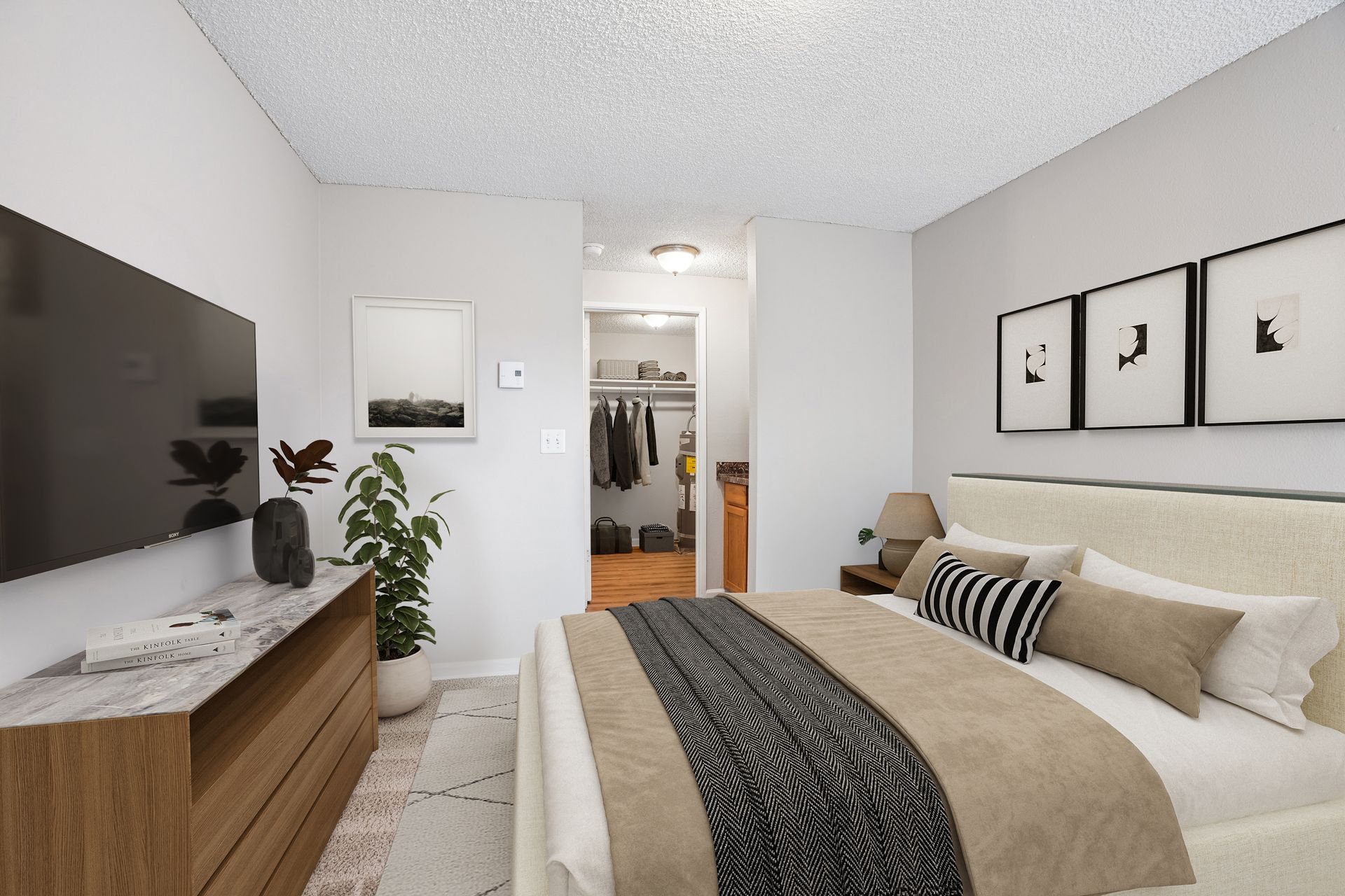 Bright bedroom with beige bed, wood dresser, wall art, and open closet in the background