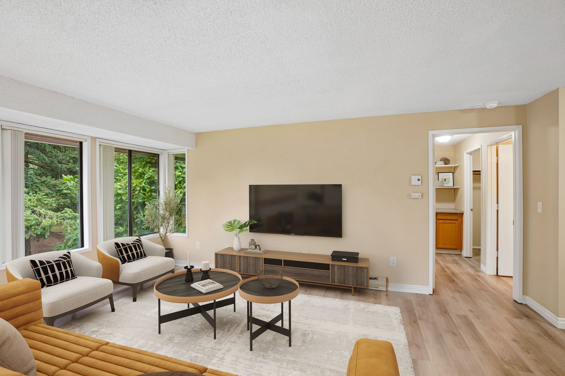 Bright living room with sofa, TV, coffee tables, large windows, and hallway view
