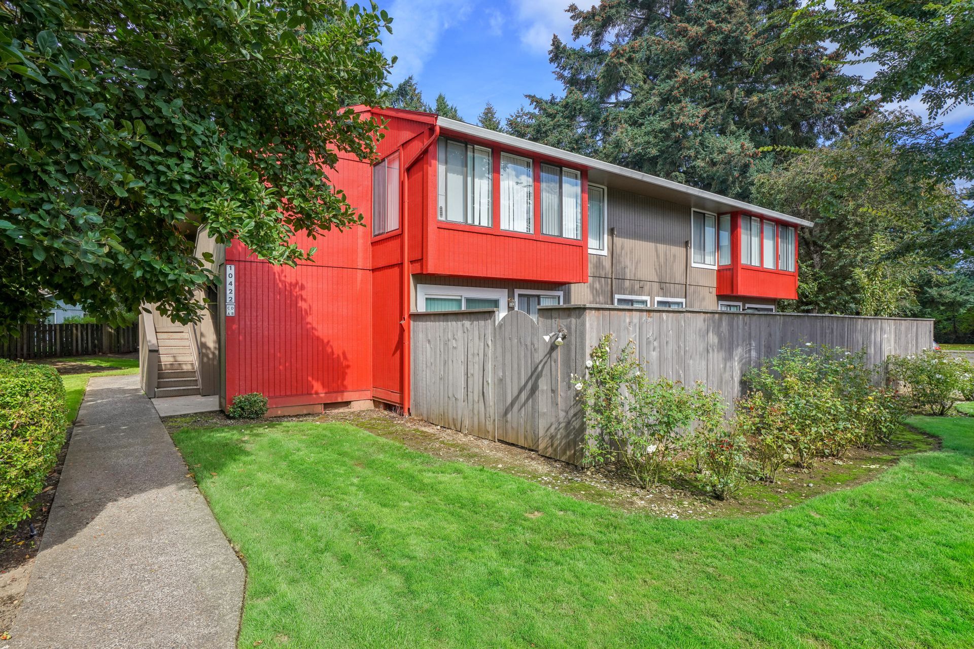 Exterior of a two-story apartment building with red accents and a wooden privacy fence.