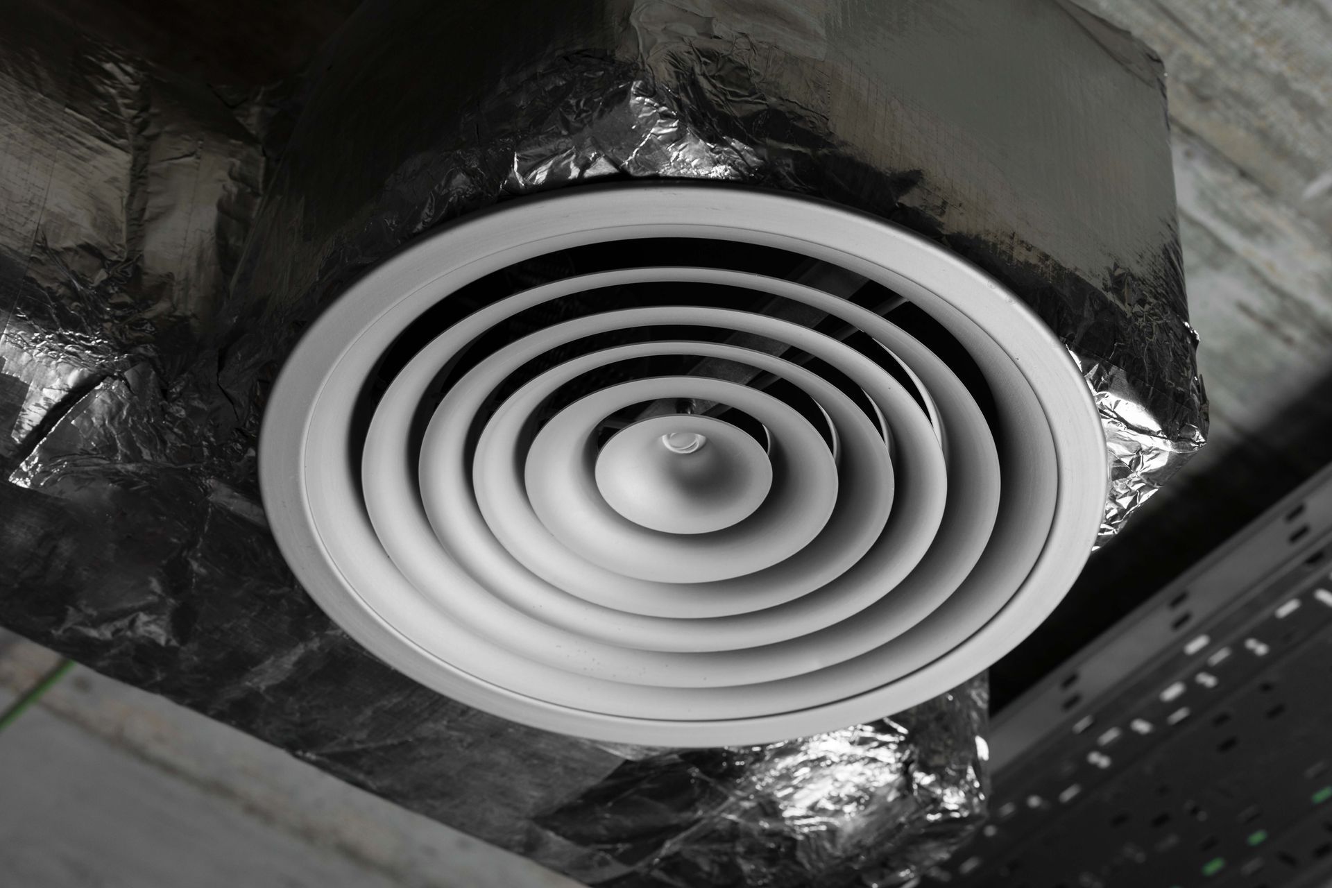 Witte ronde ventilatieopening in een kanaal bekleed met folie-isolatie.
