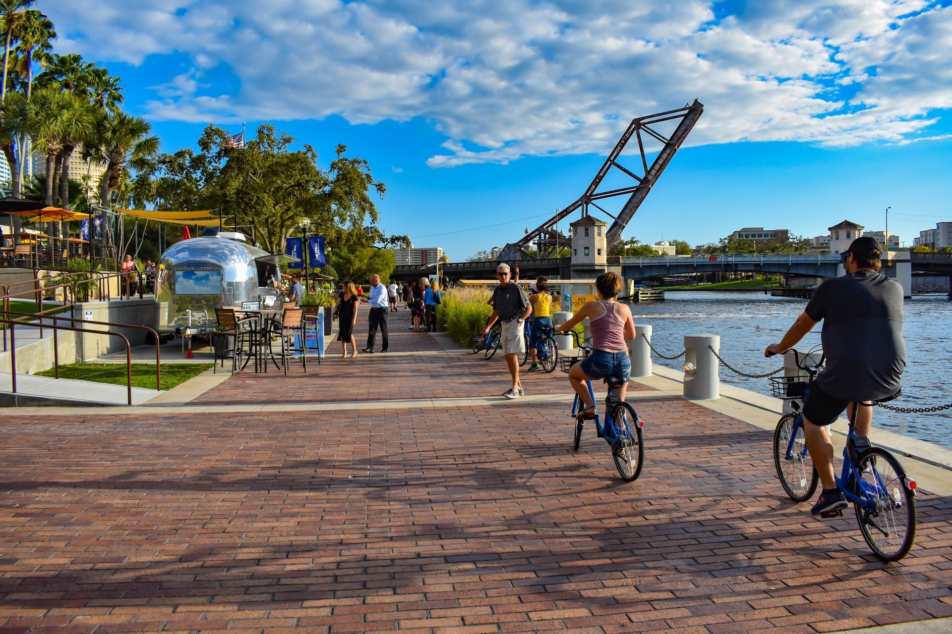 people riding bikes on a brick sidewalk near a river