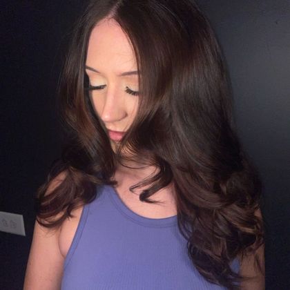 Woman with long dark hair looking down in a purple top against a dark background