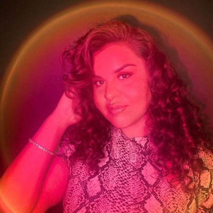 Portrait of a woman with curly hair under pink-red neon lighting, wearing a snake-print top