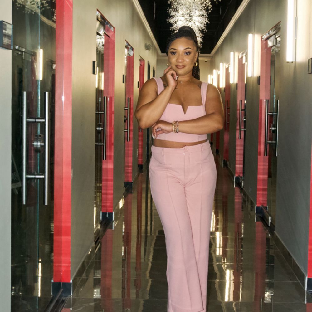 Woman in pink outfit posing in a hallway with glossy floors and red wall accents