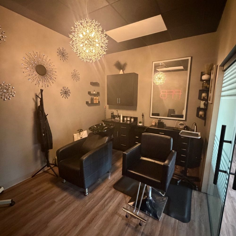 Modern hair salon interior with two black chairs, mirror stations, wall art, and warm lighting