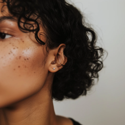 Close-up profile of a person with curly hair and freckles, wearing a small earring