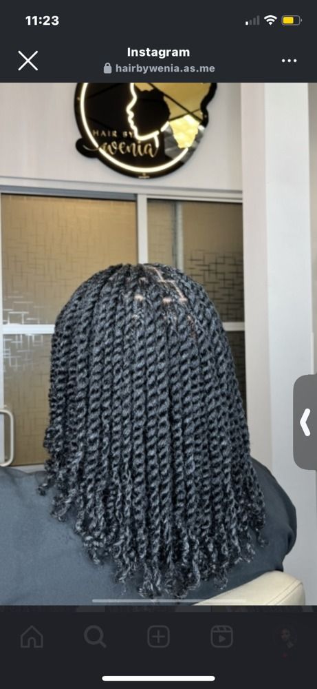 Back of a person with long black twisted braids in front of a salon mirror and logo sign