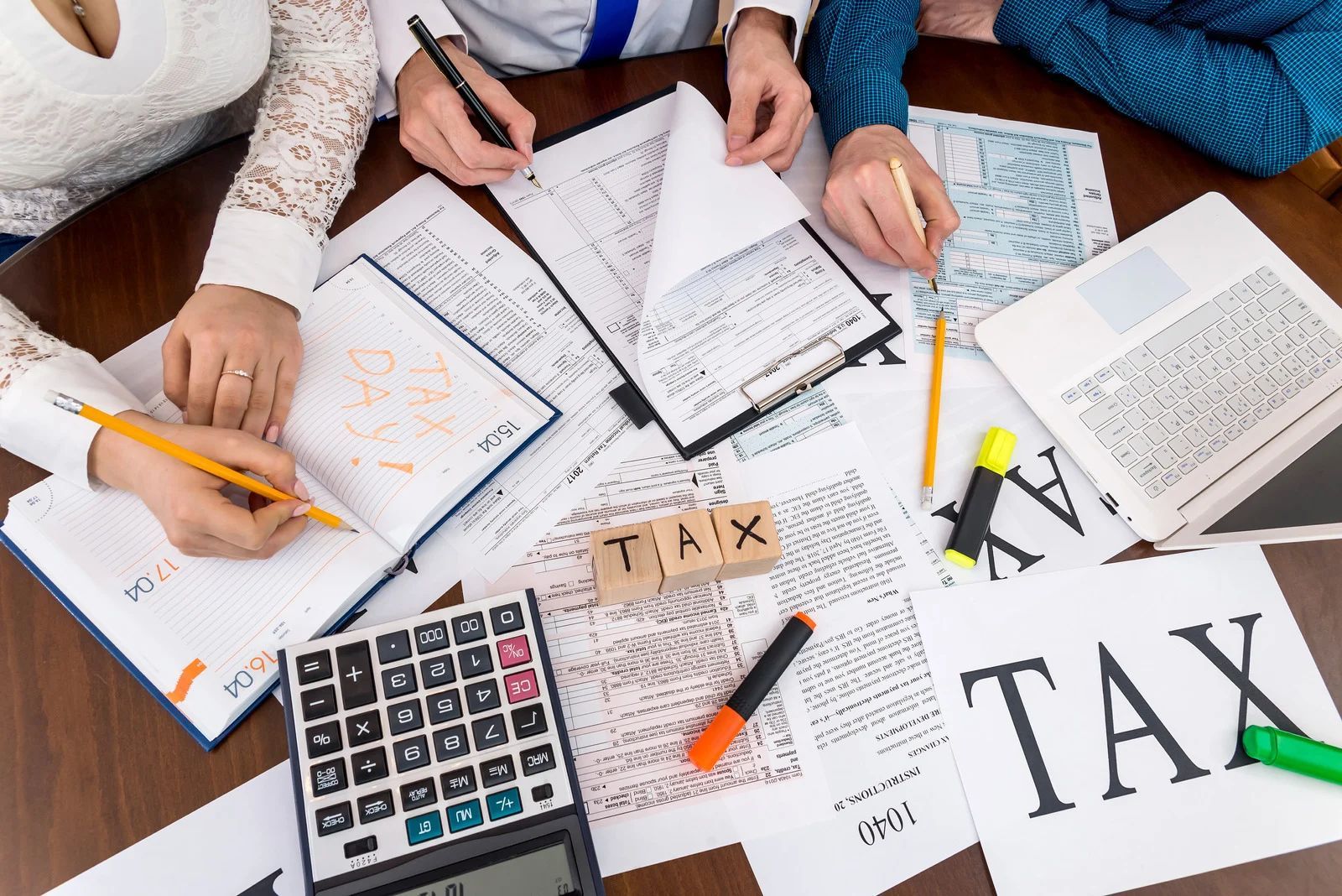 People reviewing tax documents with calculator, pens, and forms on a desk