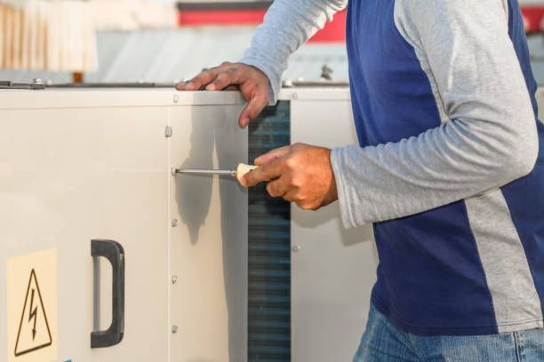 Person using a screwdriver to work on a large, white appliance outdoors.