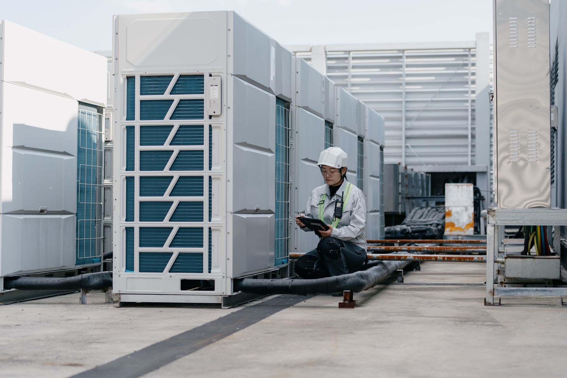 Engineer inspecting rooftop HVAC units with tablet in hand. Worker in hard hat inspecting rooftop HVAC units.