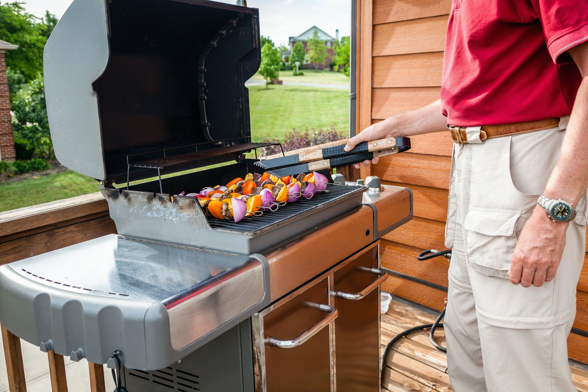 Staff And Customer — Kalamazoo, MI — Suburban Heating & Air Conditioning Man grilling kebabs on a barbecue grill on a wooden deck.