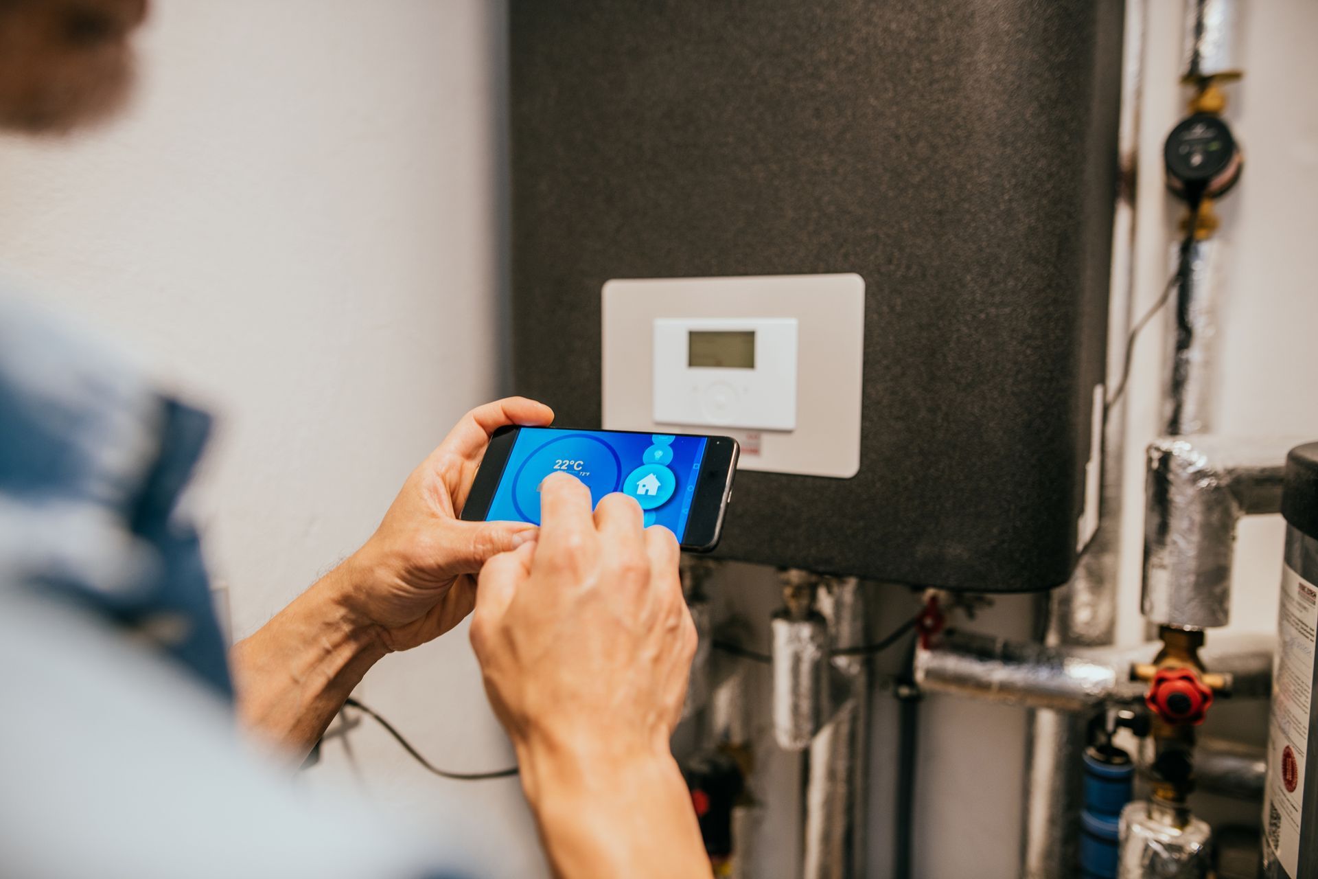 Person using smartphone to control a heating system, indoors.