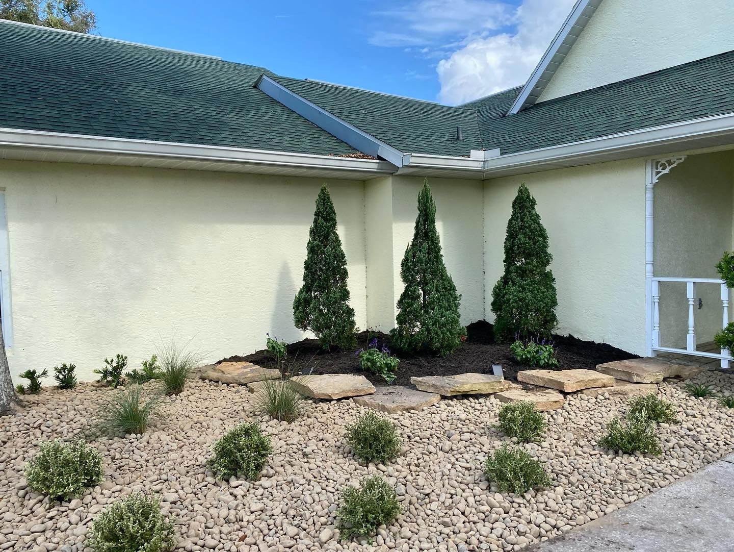 A white house with a green roof and a garden in front of it.