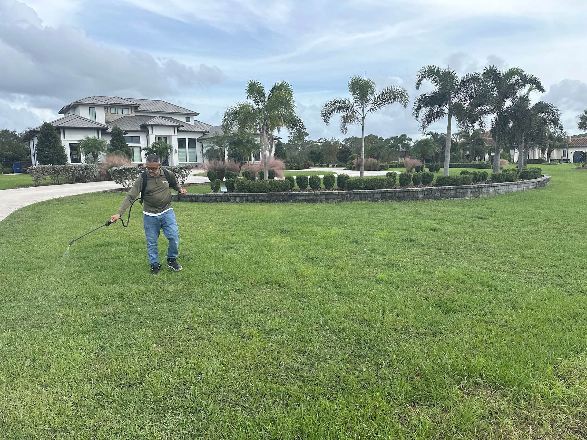 A man is standing in a lush green field in front of a large house.