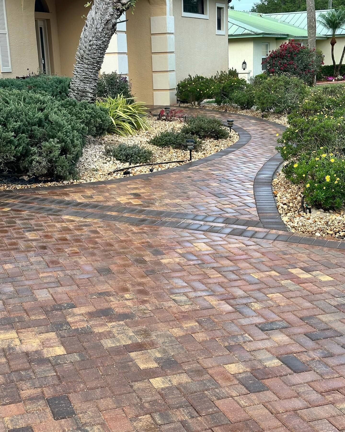 A brick driveway leading to a house with a tree in the background