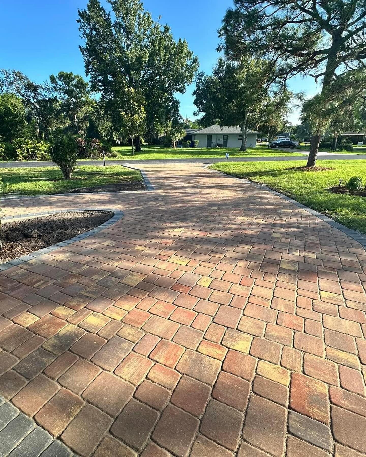 A brick driveway leading to a house with trees in the background.