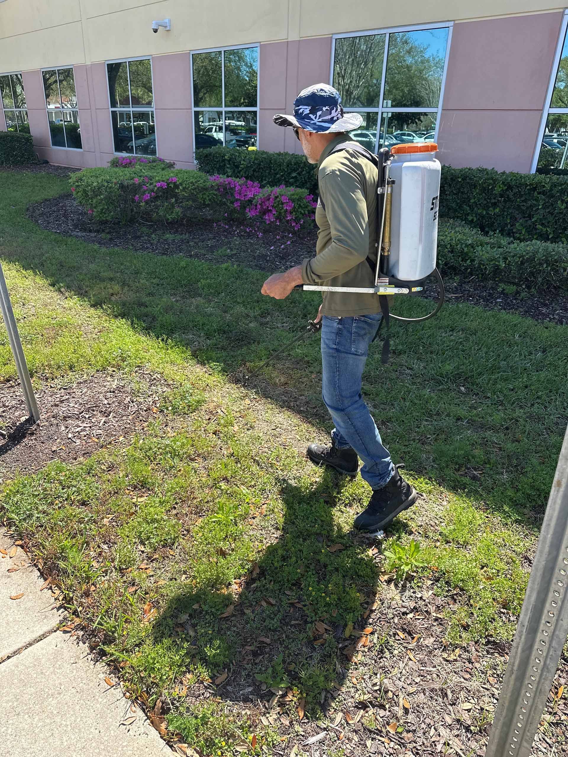 A man is spraying grass in front of a building.
