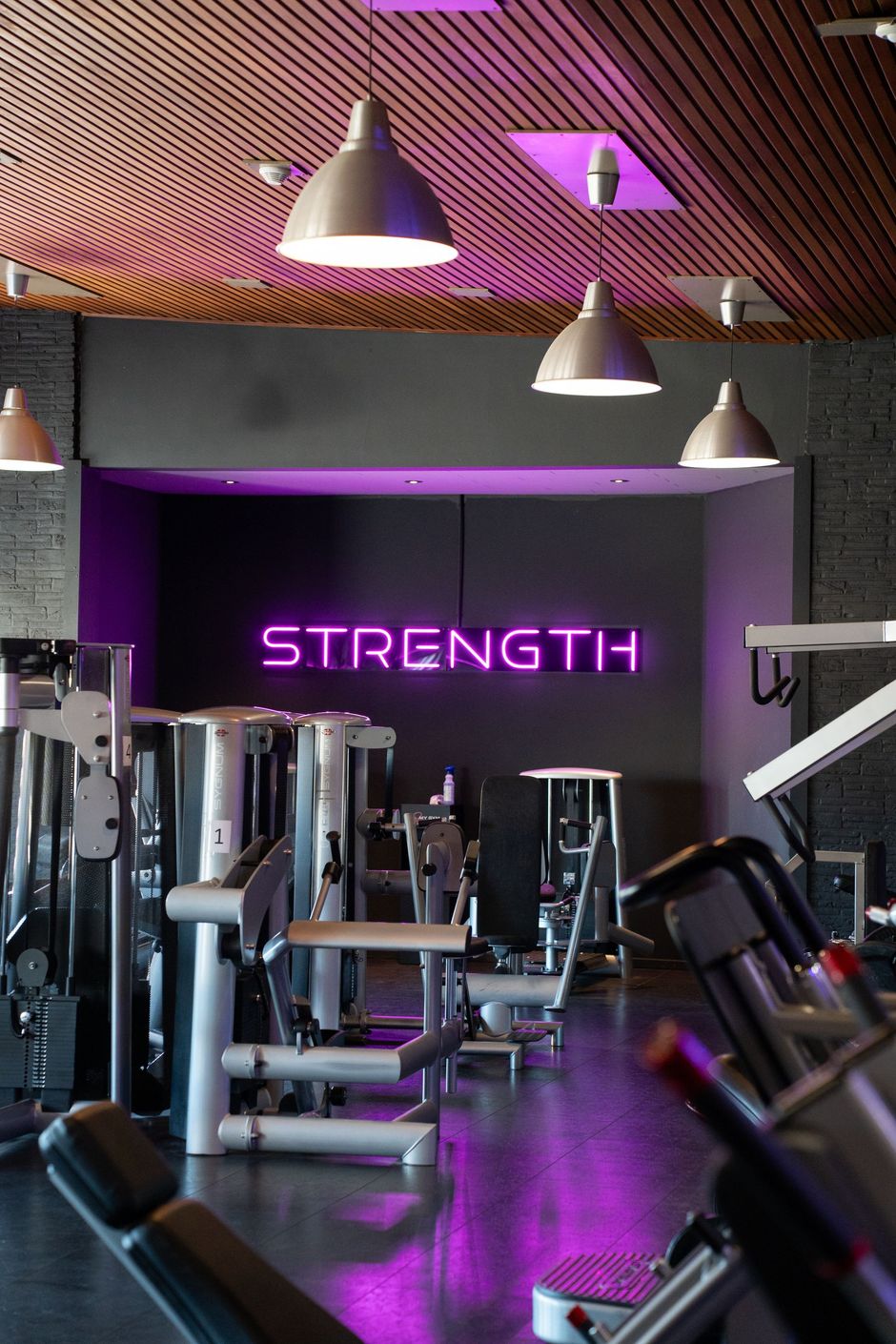 Modern fitnesscentrum met gewichtsapparaten, paarse verlichting en een neonbord met de tekst 