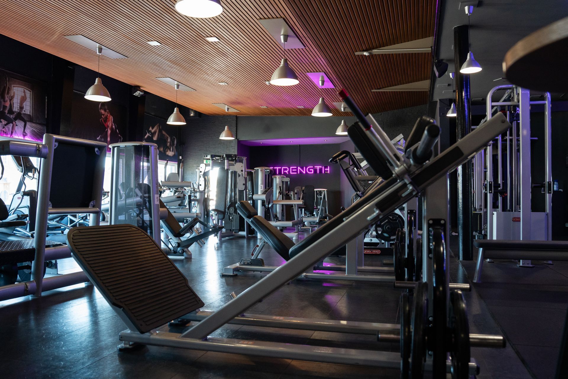 Modern fitnesscentrum met gewichtsapparaten, spiegels en paarse accentverlichting.