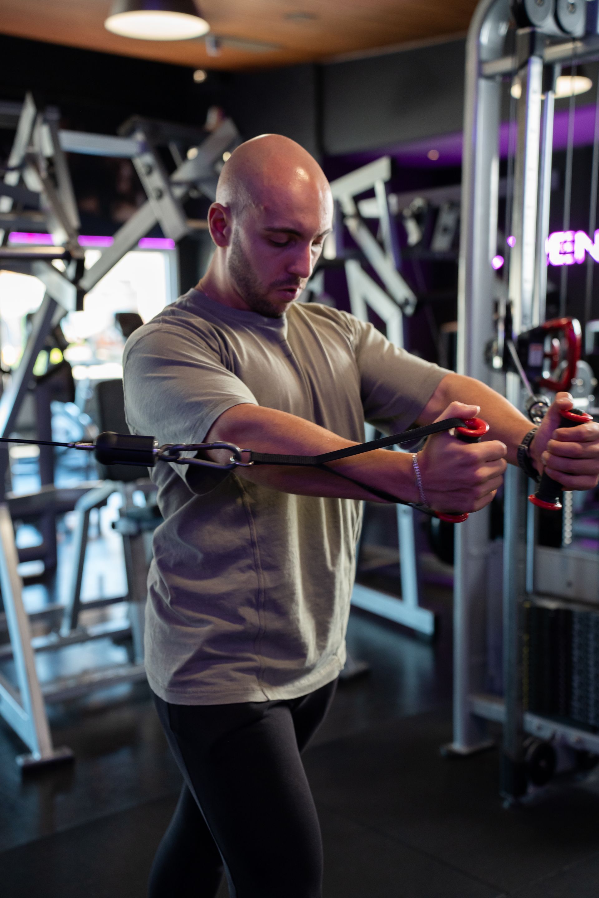 Een man, gekleed in een grijs shirt en zwarte legging, stelt de handgreep van een kabelmachine in een sportschool af.