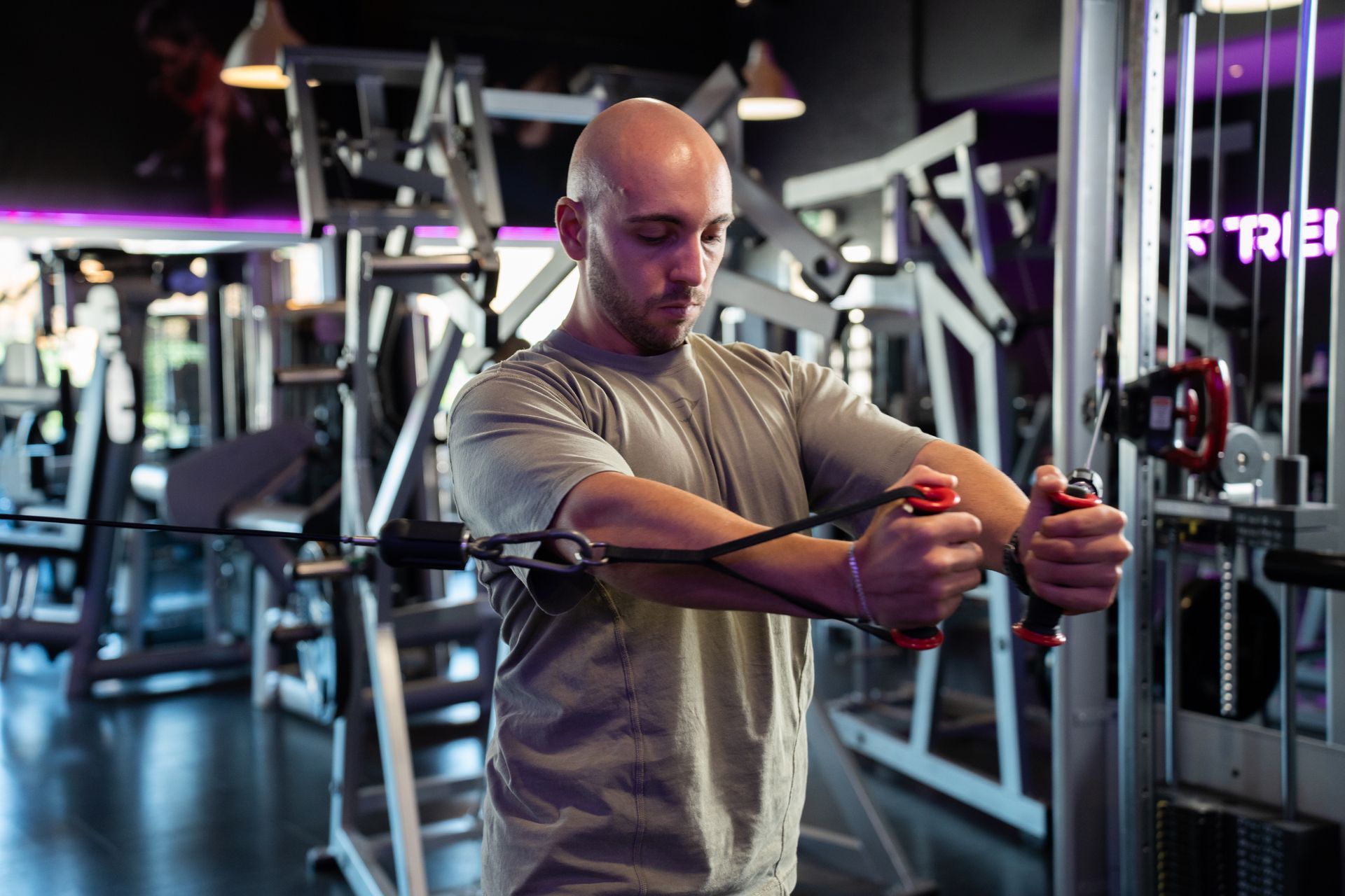 Een man traint met een kabelmachine in een sportschool en duwt de handgrepen met een geconcentreerde houding naar voren.