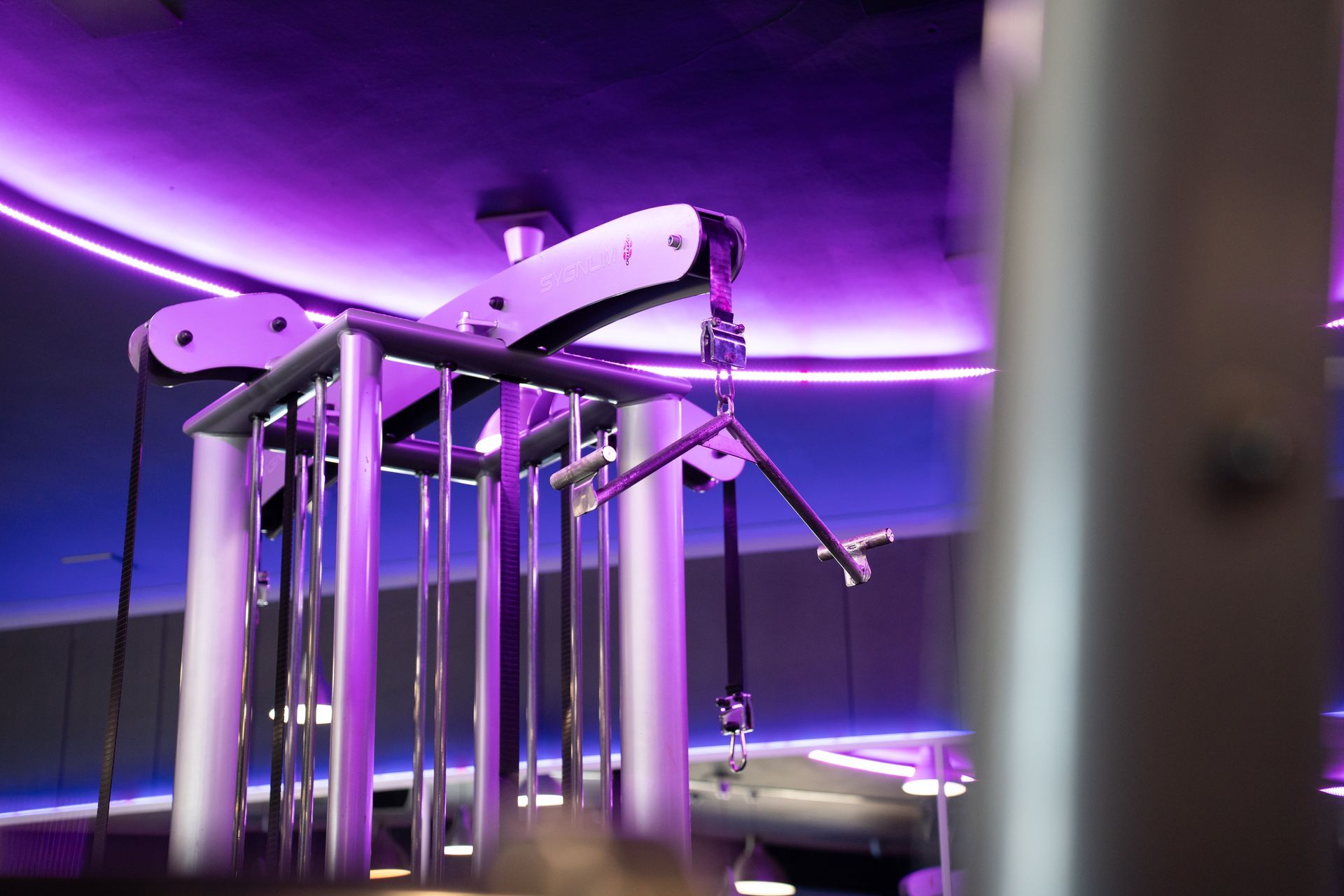 Paars verlichte kabelmachine voor in de sportschool met chromen stangen en katrollen.