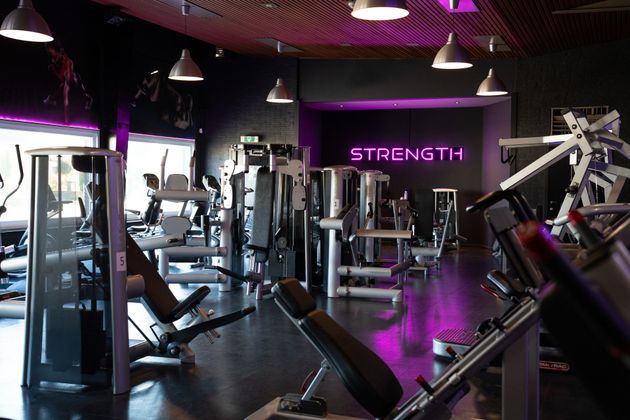 Modern fitnesscentrum met gewichtsapparaten, paarse verlichting en een neonbord met de tekst 