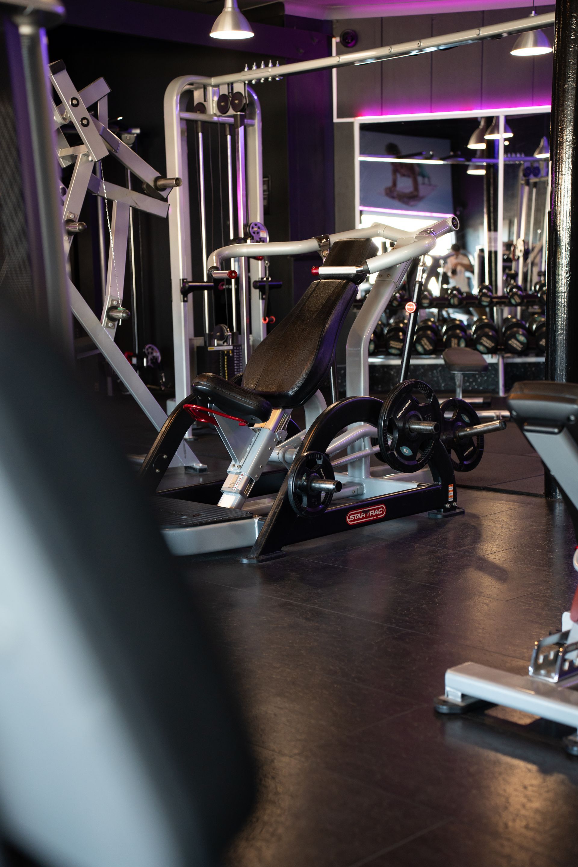 Interieur van een sportschool met een zwarte hometrainer, gewichtsapparaten en paarse verlichting.