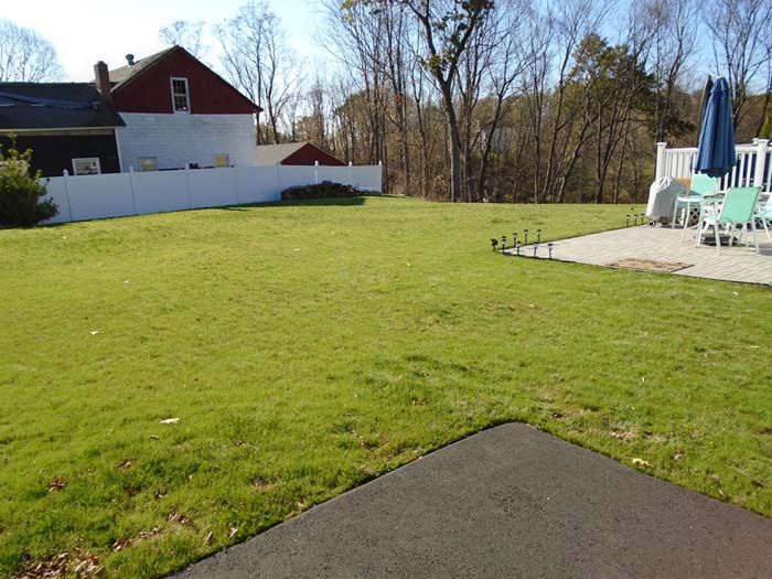 A lush green yard with a white fence and a red house in the background