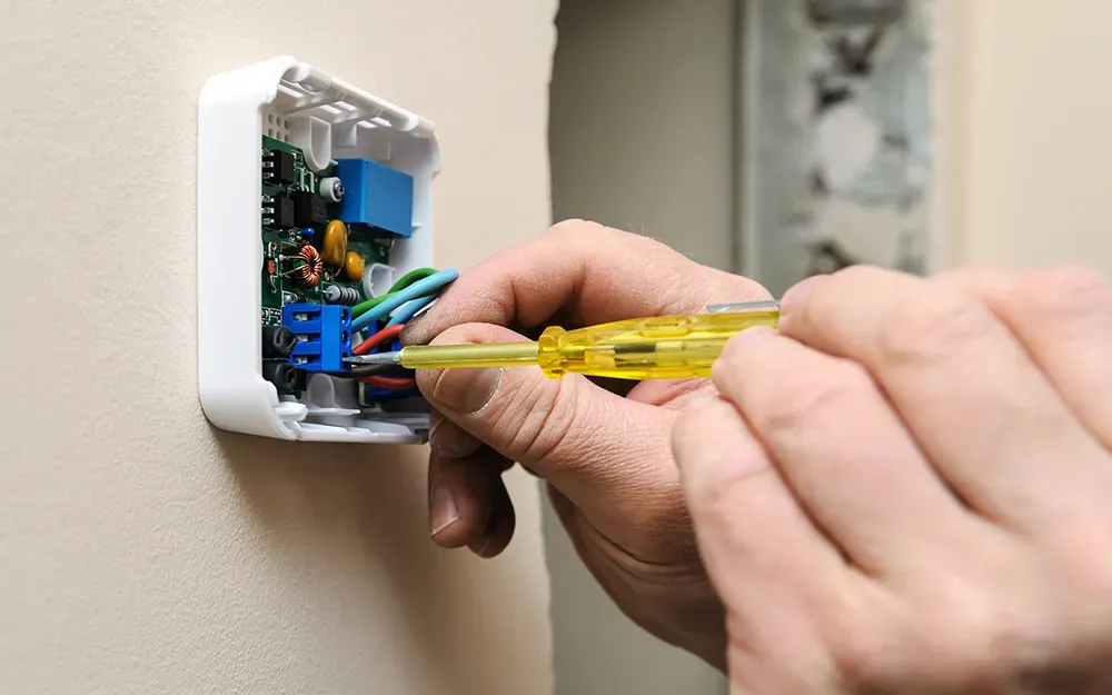 A person is installing a thermostat on a wall with a screwdriver. A person is installing a thermostat on a wall with a screwdriver.