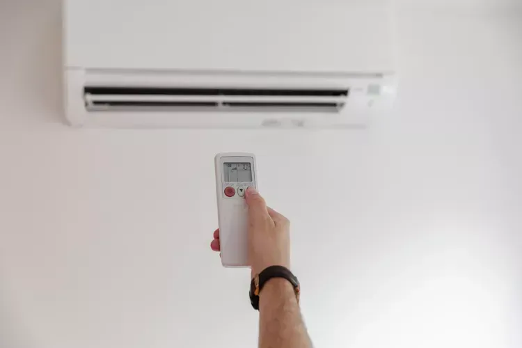 A person is holding a remote control in front of an air conditioner.