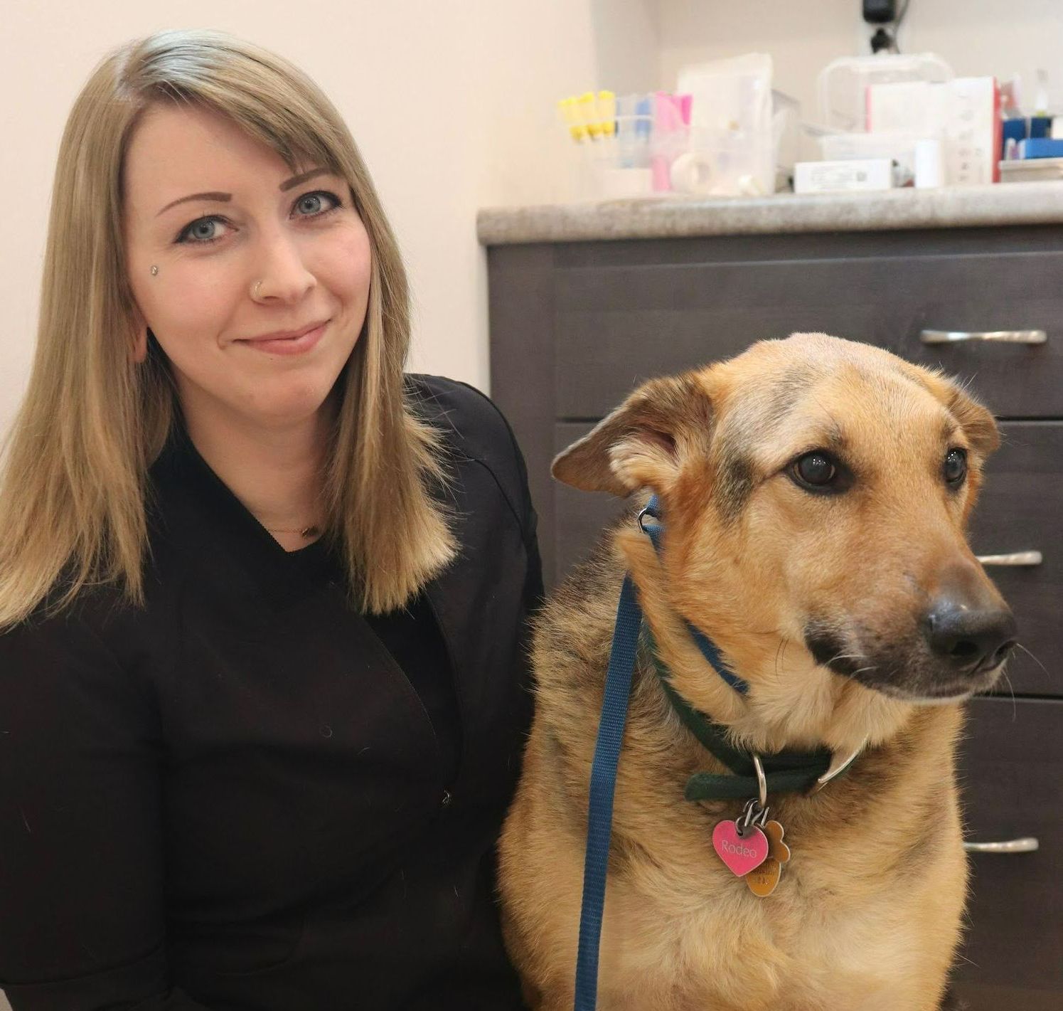 A woman sitting next to a brown dog on a leash