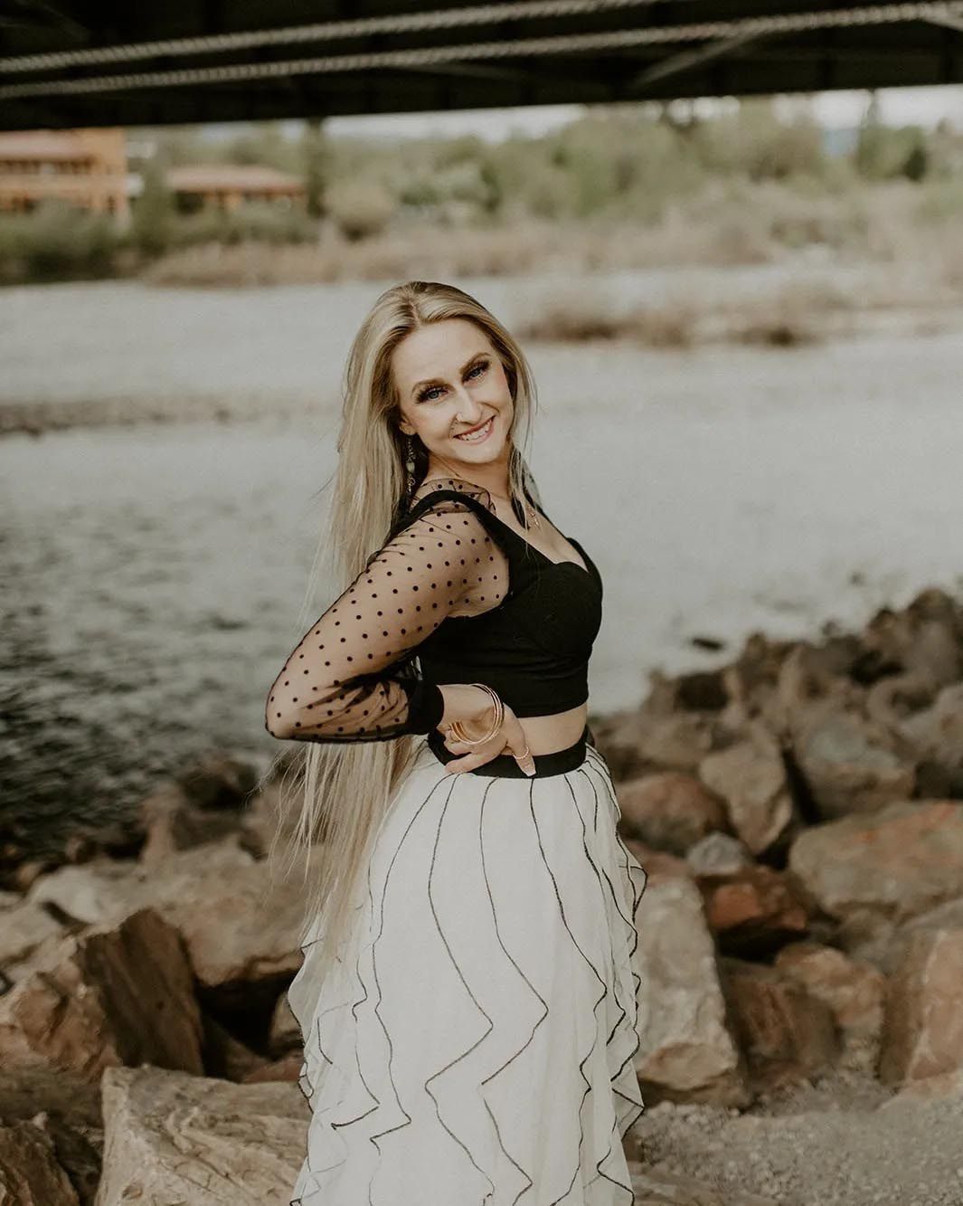 A woman in a black top and white skirt is standing next to a river.