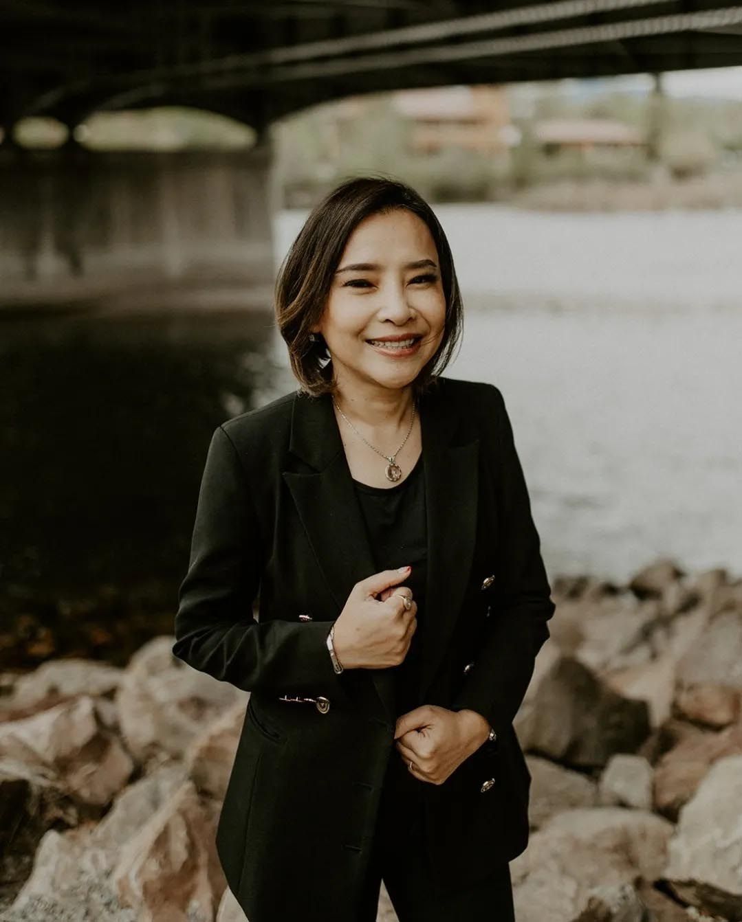 A woman in a black suit is standing next to a body of water.