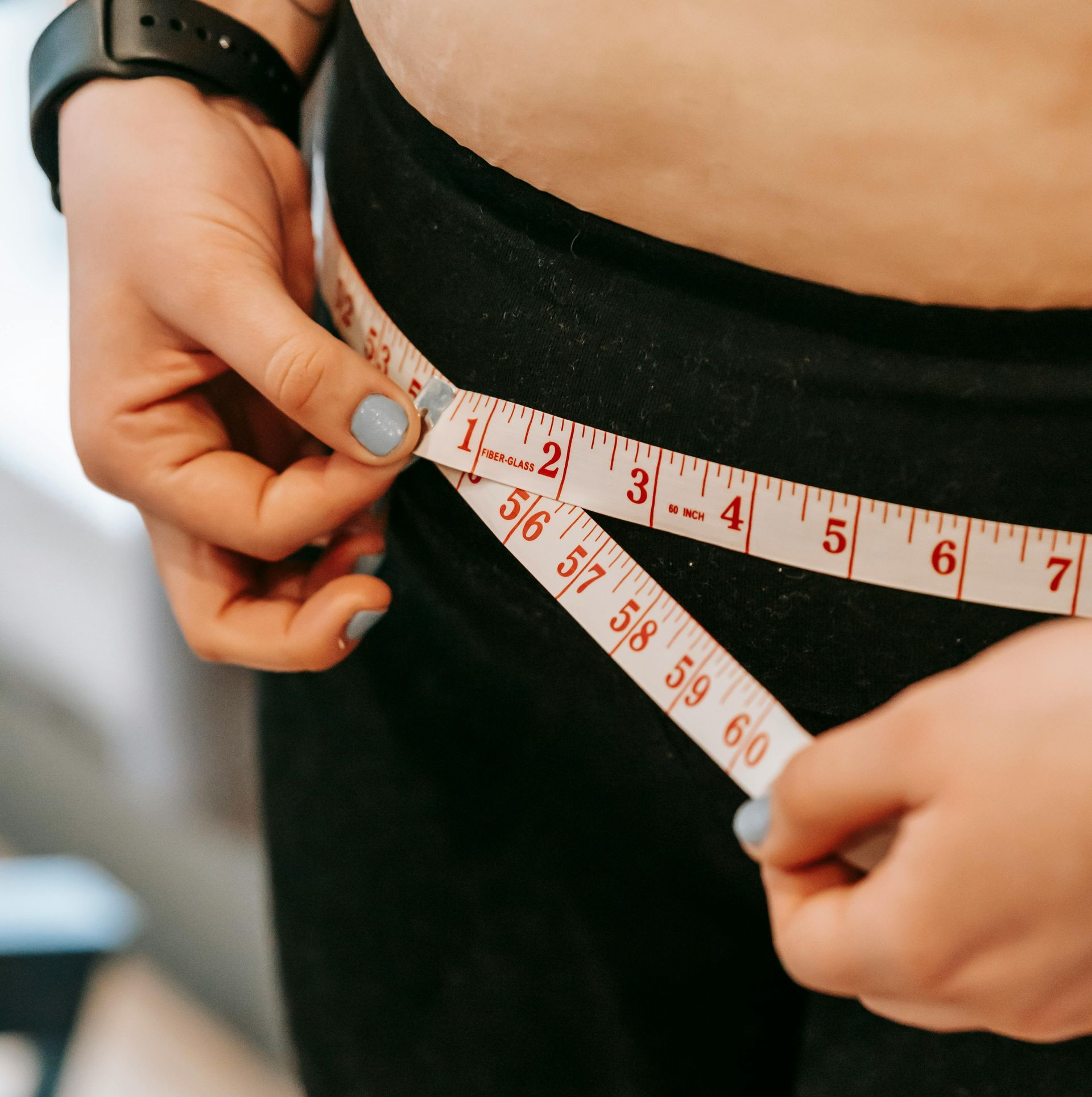 Person measuring waist with a white and red tape measure over black pants.