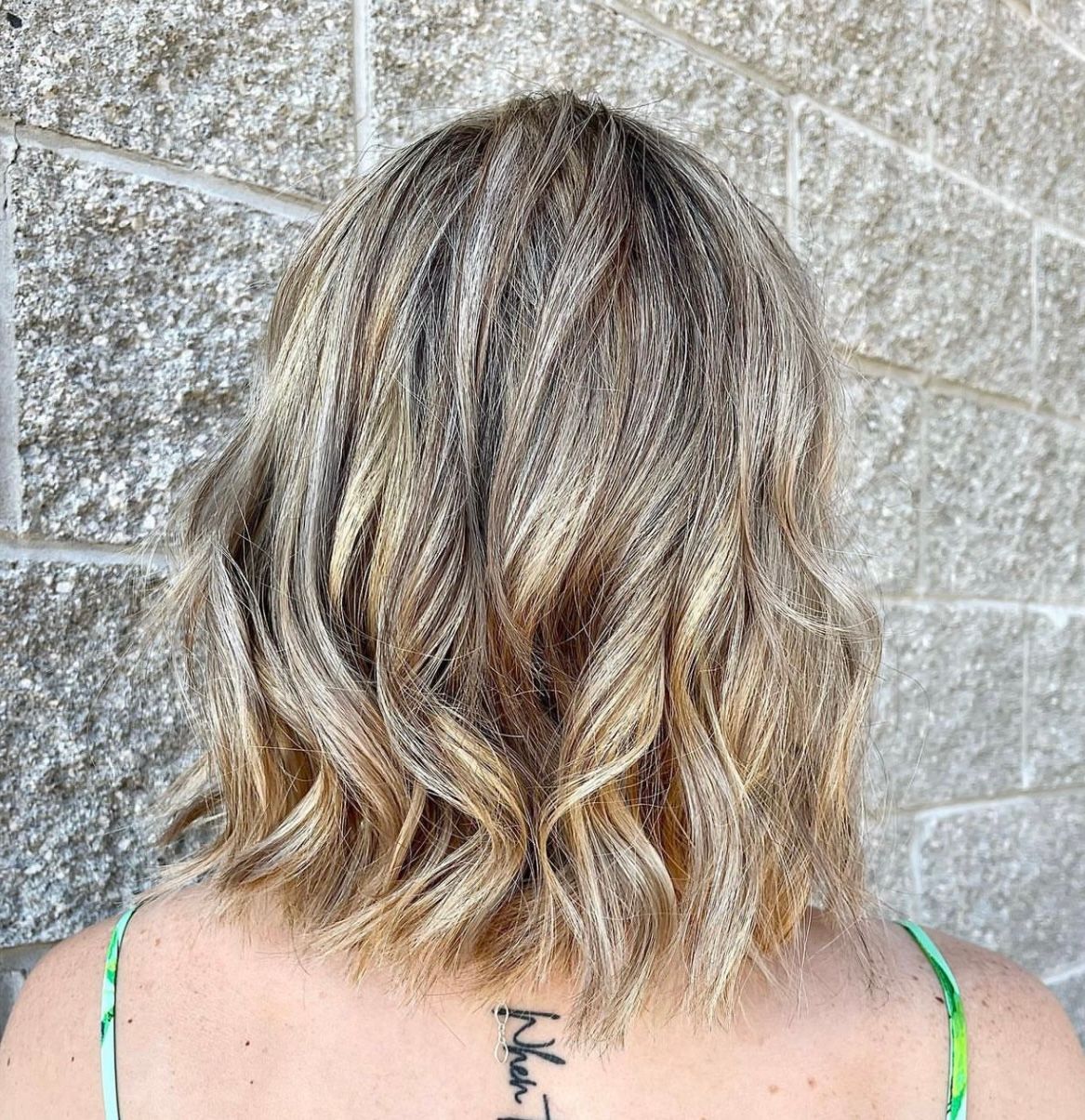 A woman with blonde hair and a tattoo on her back is standing in front of a brick wall.