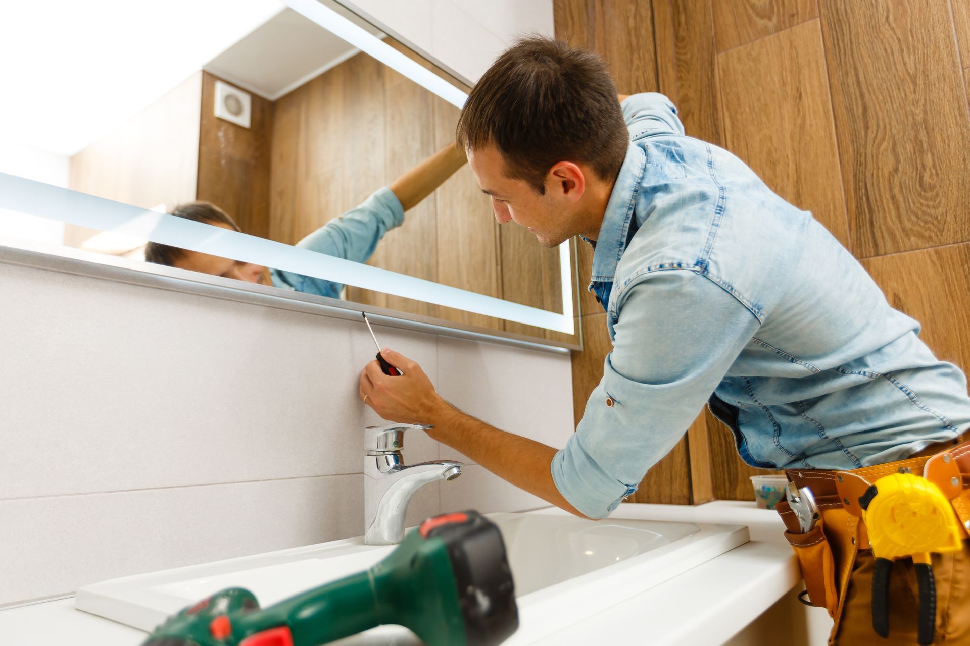 Technician installing a bathroom mirror above a white vanity with a drill and tools nearby