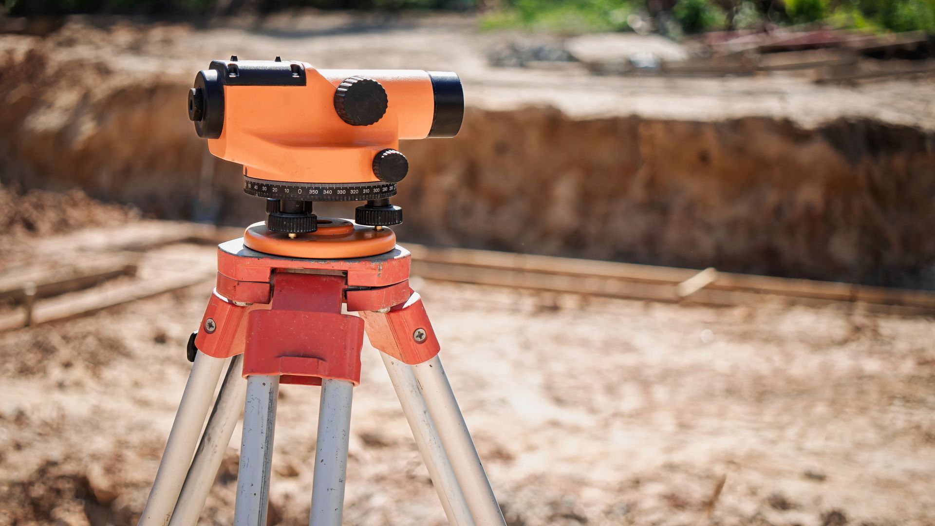 Orange surveying level on a tripod at a construction site