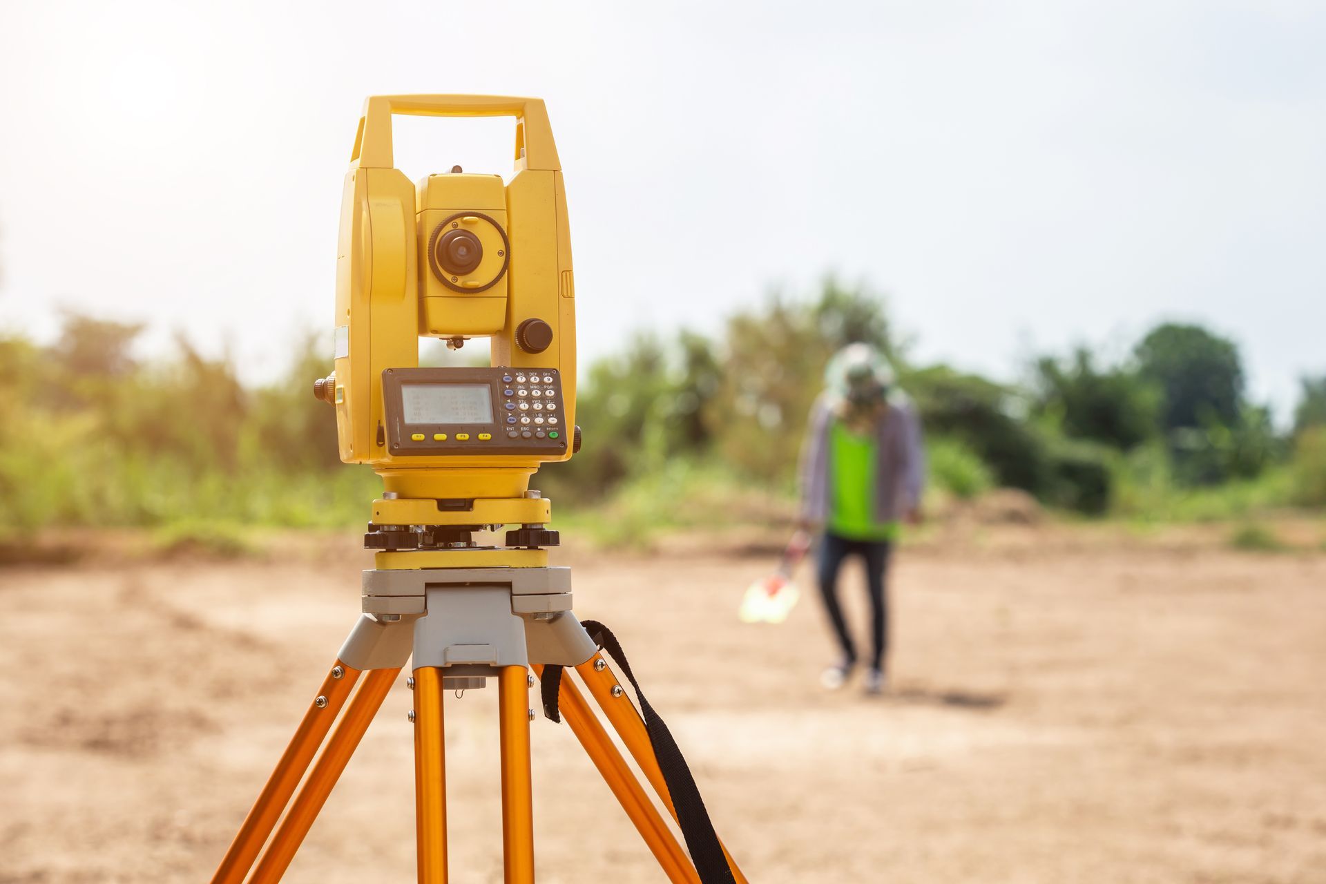 Yellow surveying instrument set on a tripod at a construction site with a worker in background. Yellow surveying instrument set on a tripod at a construction site with a worker in background.